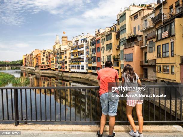 a pair of young women looking from on a bridge, cathedral and houses on onyar riverbank, spain, catalonia, girona. - fiume onyar foto e immagini stock