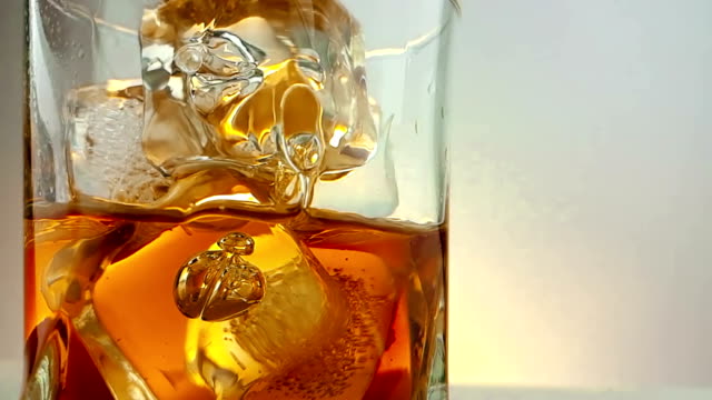 close-up of  barman pouring whiskey in the drinking glass with ice cubes on warm white background, time of relax drink with whisky