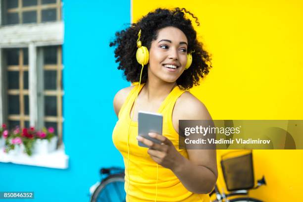 afrikaanse vrouw met gele hoofdtelefoon met behulp van slimme telefoon - fashion pretty woman listening music in headphones with smartphone colorful stockfoto's en -beelden