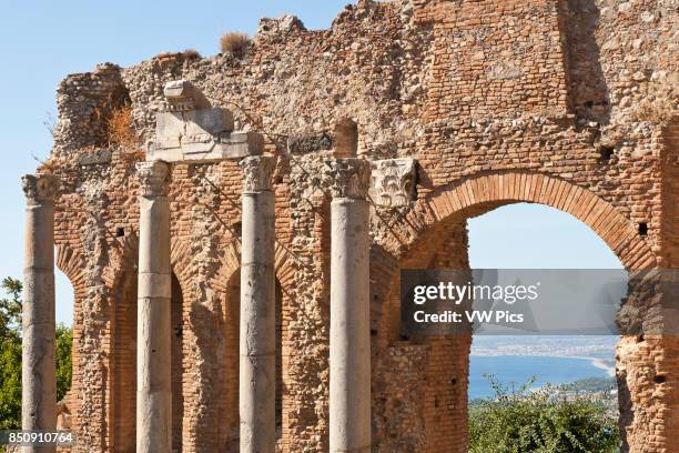 Columns and wall inside the Greek Theatre, and view of Golfo Di Naxos, Taormina, Sicily, Italy.