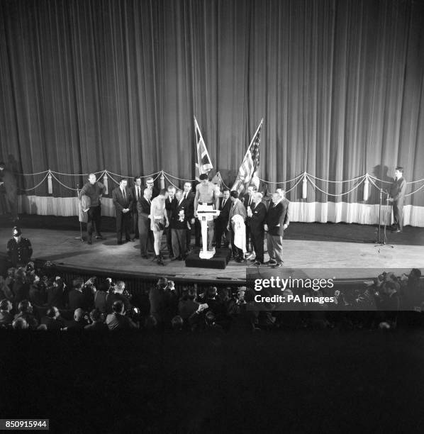 American heavyweight Cassius Clay on the scales in front of the American and British flags, and British challenger Henry Cooper talking with Teddy...