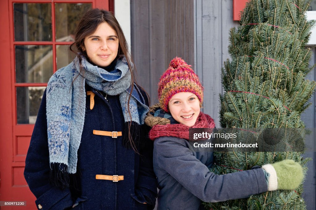 Duas irmãs com recentemente cortada a árvore de Natal na frente no exterior da casa.