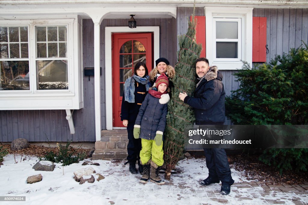 Familienbild mit frisch geschnittenen Weihnachtsbaum vor Haus im Freien.