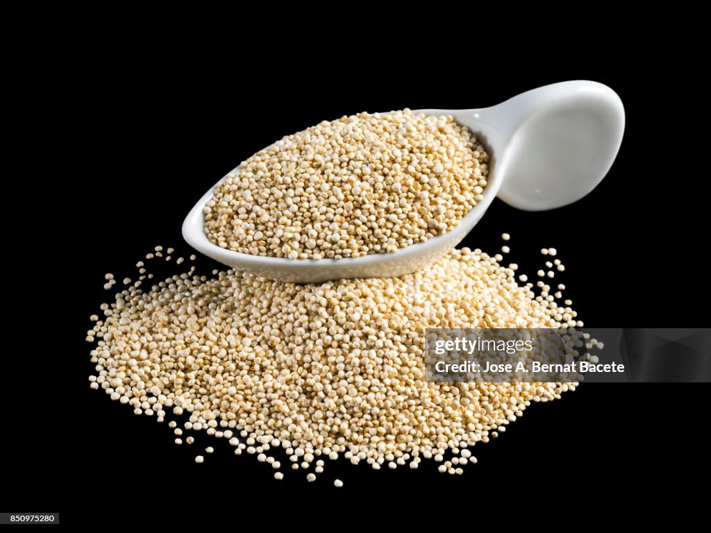 White porcelain spoon full of Quinoa grains on a black background