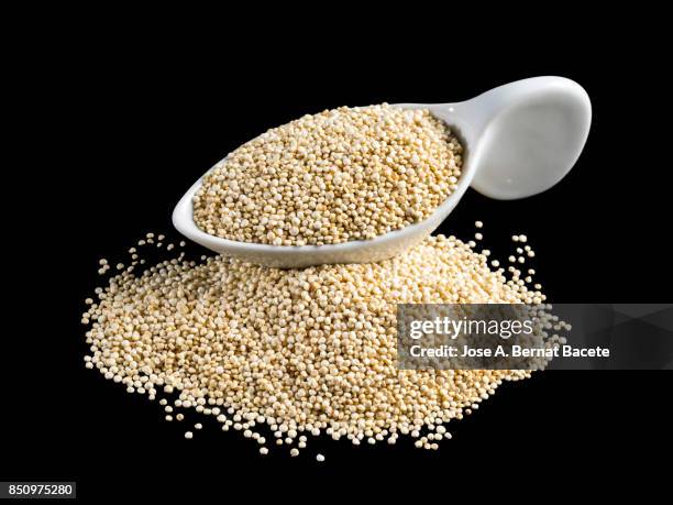 white porcelain spoon full of quinoa grains on a black background - spion stock pictures, royalty-free photos & images