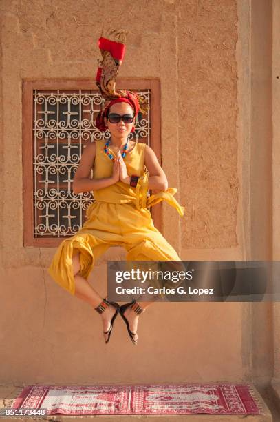 asian girl wearing turban jumps on carpet with praying hands - 空飛ぶ絨毯 ストックフォトと画像