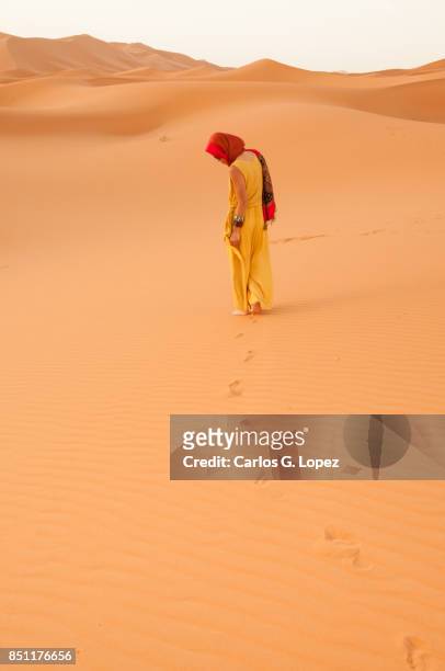 girl with head scarf walking on the sahara desert looking at her footprints - hot arabic girl stock pictures, royalty-free photos & images