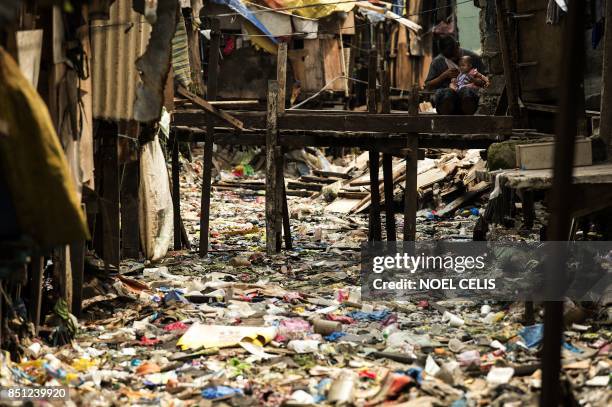 Man holds a baby on a bridge over a garbage filled creek in Manila on September 22, 2017. - Giant Western consumer products brands led by Nestle,...