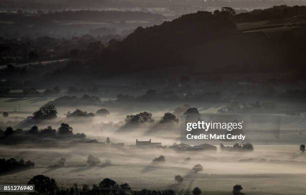 Farm house is surrounded by early morning mist lingering in fields as the autumn sun rises over the Somerset Levels as viewed from Glastonbury Tor...