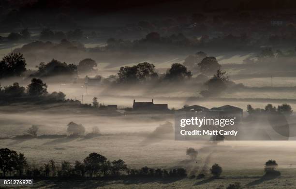 Farm house is surrounded by early morning mist lingering in fields as the autumn sun rises over the Somerset Levels as viewed from Glastonbury Tor...