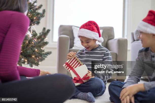 ein kleiner junge öffnet strahlend ein weihnachtsgeschenk - schocktaktik stock-fotos und bilder