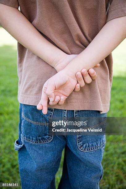 boy crossing fingers behind back - kid middle finger stock-fotos und bilder