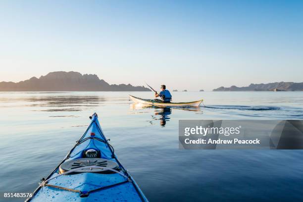 a man is paddling a sea kayak in calm ocean. - kayak stock pictures, royalty-free photos & images