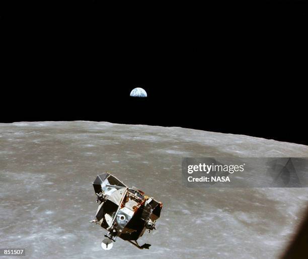 With a half-Earth in the background, the Lunar Module ascent stage with Moon-walking Astronauts Neil Armstrong and Edwin Aldrin Jr. Approaches for a...