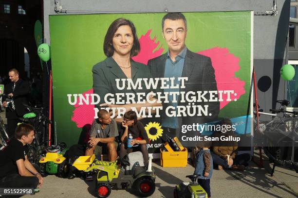People sit next to an election campaign billboard that shows German Greens Party co-lead candidates Cem Oezdemir and Katrin Goering-Eckardt outside a...