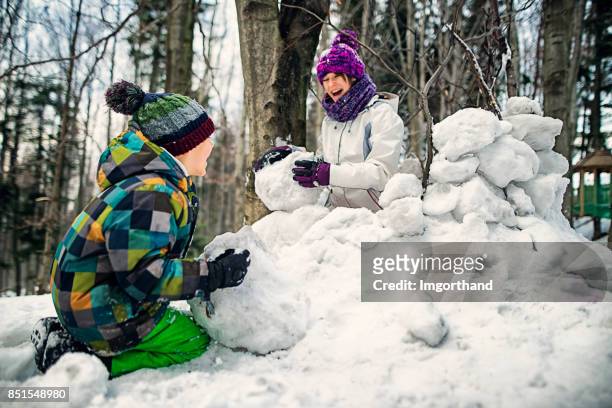 brother and sister having fun building a snow fortress in forest - fort stock pictures, royalty-free photos & images