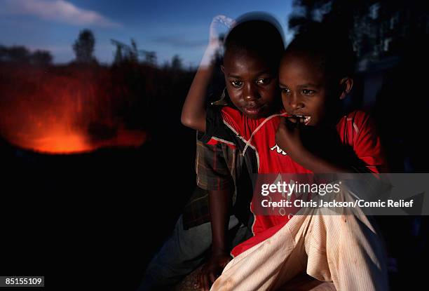 Children sit next to a burning rubbish pit as GMTV presenter Ben Shepard visits Mkombozi project for street children on February 26, 2009 in Moshi...