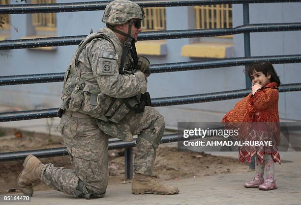 Soldier kneels as he speaks to a little Iraqi girl as he and other secure the area along with Iraqi soldiers for the arrival of a shipment of sports...