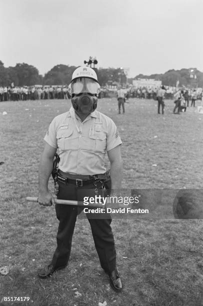 Portrait of a police officer in a gas mask as he stands with a billy club in his hands during the 'Honor America Day Smoke-In' thrown by marijuana...