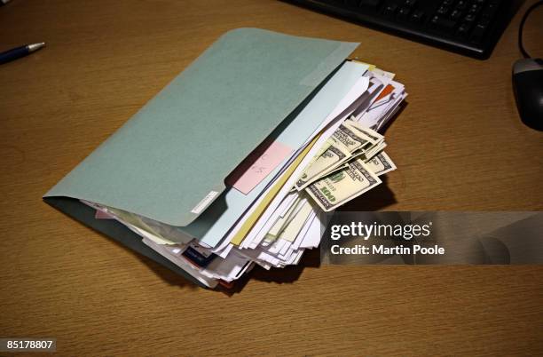 folder on desk with 100 dollars bills stuck in it - corruption stockfoto's en -beelden