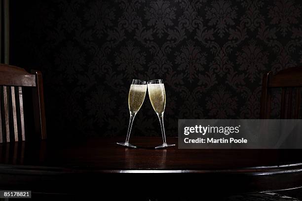 two champange glasses leaning to kiss on table - champagneglas stock-fotos und bilder