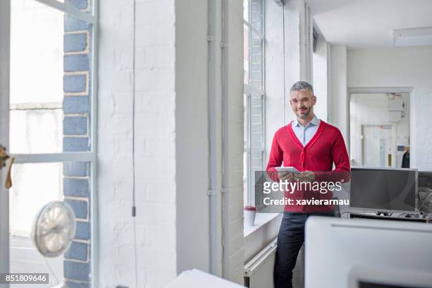 smiling businessman standing with tablet at office - red cardigan sweater stock pictures, royalty-free photos & images