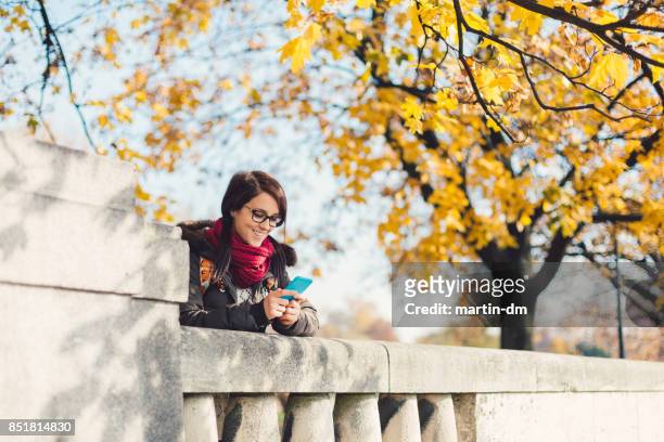 smiling woman texting in the park during autumn - krakow park stock pictures, royalty-free photos & images