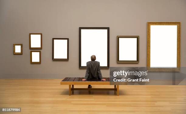 man enjoying looking at blank frames on wall. - wooden bench stock pictures, royalty-free photos & images