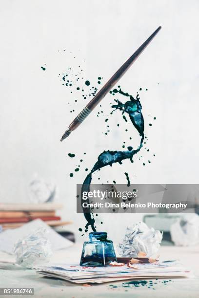 spilled ink flying above inkwell in a spiraling splash with tiny drops and flying pen on a light background. still life with writer workplace. creative writing concept. - story telling in the workplace stockfoto's en -beelden