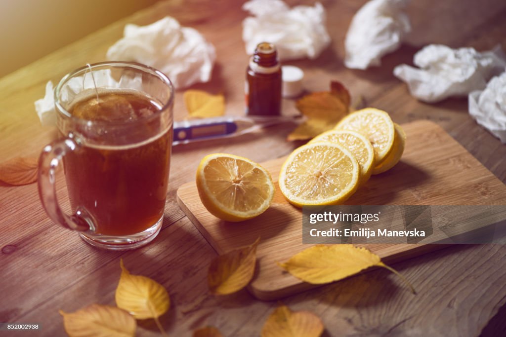 Thermometer, medicine, tissue and a cup of tea on wooden background