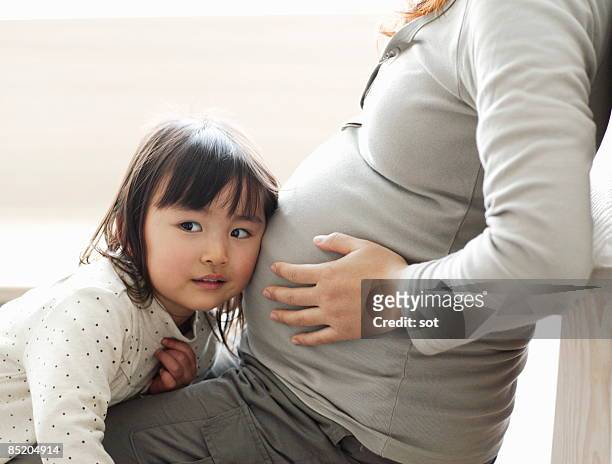 little girl listening to pregnant mother's abdomen - asian woman pregnant stockfoto's en -beelden