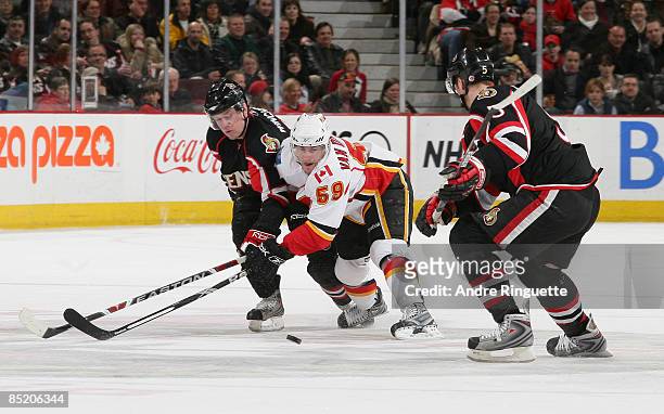 Jesse Winchester and Christoph Schubert of the Ottawa Senators defend as David Van der Gulik of the Calgary Flames battles for puck possession at...