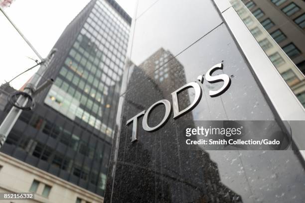 Close-up of sign with logo for Tod's upscale boutique shoe store, with building visible in the background, on Madison Avenue in Manhattan, New York...