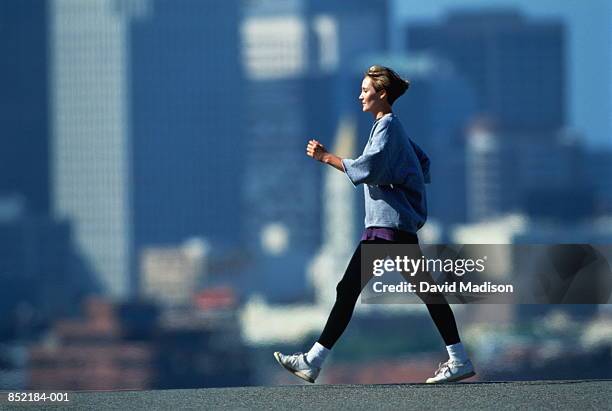 woman speed walking in fore of city skyline - walking side view stock-fotos und bilder