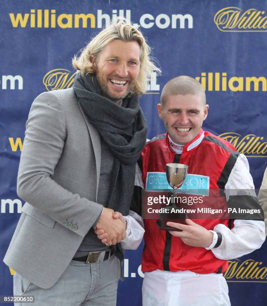 Robbie Savage hands out a trophy to jockey Tony Hamilton who rode Hi There to victory in The William Hill Download The App Handicap Stakes during Day...