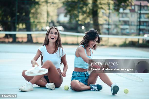 two smiling females posing on tennis court and juggling with racket and ball - tennis outfit stock pictures, royalty-free photos & images