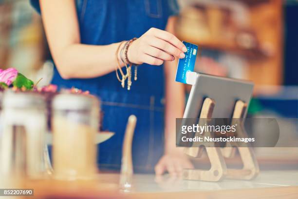 female owner swiping credit card using digital tablet in cafe - swipe stock pictures, royalty-free photos & images
