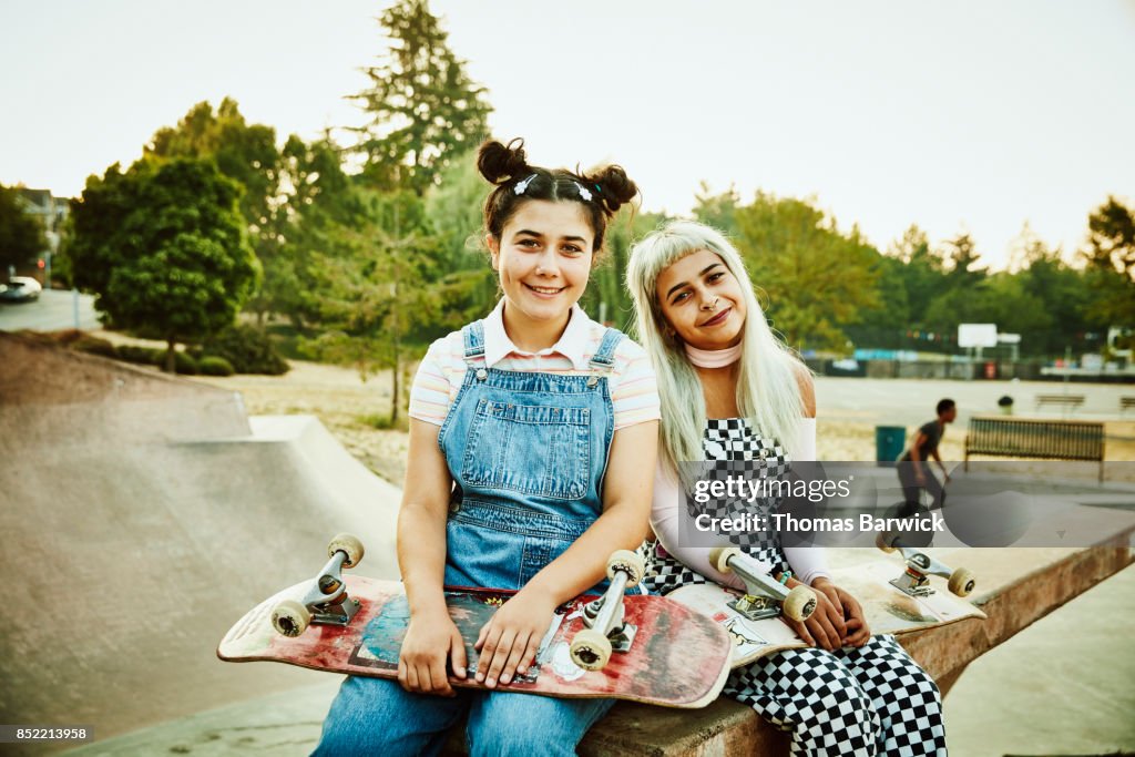 Portrait of smiling friends sitting on ramp in skate park on summer morning