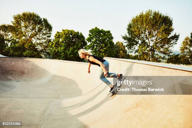 Female skateboarder skating bowl in skate park on summer morning