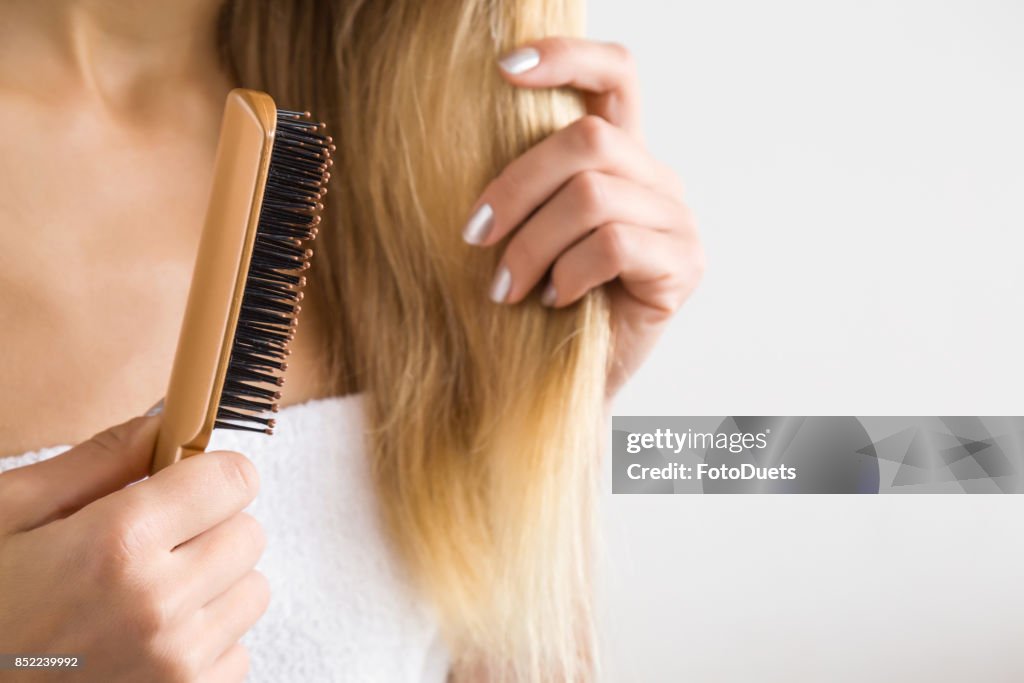 Zarte Frauenhand blonde Haare Bürsten. Kümmert sich um ein sauberes und gesundes Haar. Beauty-Salon. Leeren Platz für einen Text über dem grauen Hintergrund.