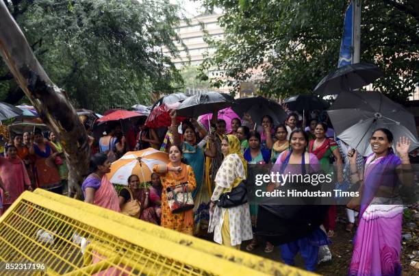 Members of Delhi Asha Workers Association holding umbrellas during the raining weather stage a protest demanding workers be considered as Government...