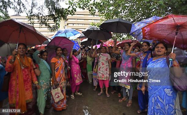 Members of Delhi Asha Workers Association holding umbrellas during the raining weather stage a protest demanding workers be considered as Government...