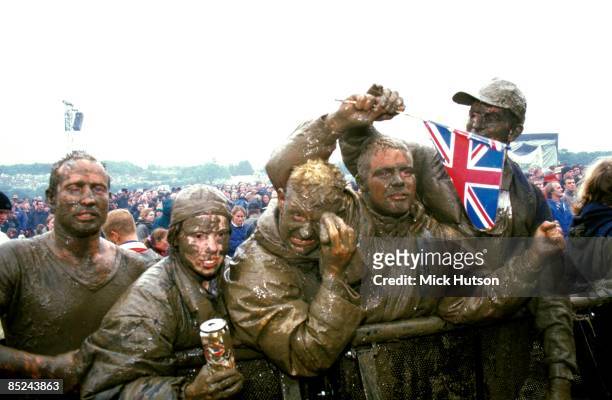 Photo of GLASTONBURY, Muddy fans in front row of audience at Glastonbury Festival, waving union jack flags