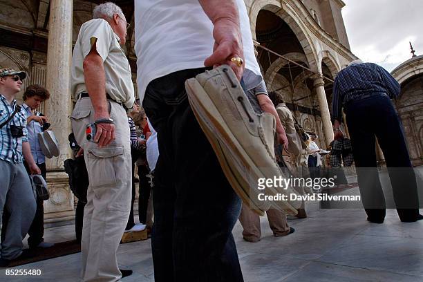 Tourists carry their shoes as they visit the 19th century Ottoman-era Muhammad 'Ali mosque, an alabaster covered landmark which dominates the...