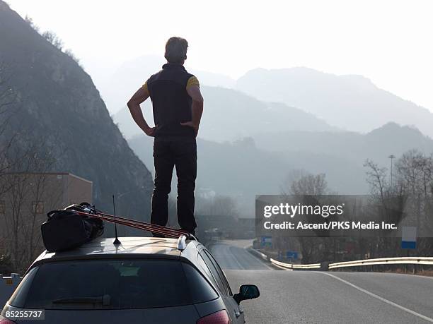 man standing on car, looking down empty road - elevate stock-fotos und bilder