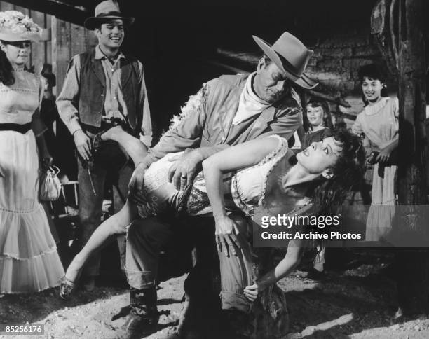 American actor John Wayne gives Maureen O'Hara a public spanking in the film 'McLintock!', watched by Stefanie Powers , his on-screen daughter and...