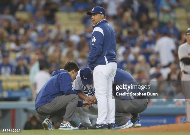 Manager Dave Roberts of the Los Angeles Dodgers stands by as trainers check the hand of starting pitcher Hyun-Jin Ryu in the third inning against the...