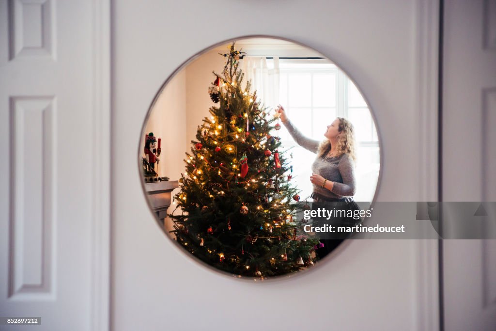 Mature woman decorating Christmas tree at home.