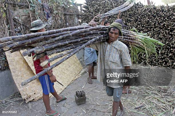 Myanmar workers carry a bundle of sugar cane at the Bargayar jetty, Kyimyindaing township in Yangon on March 6, 2009. Foreign investment in...