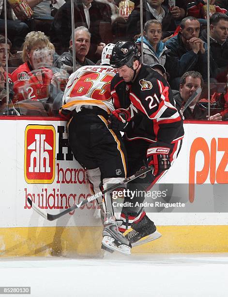 Jason Smith of the Ottawa Senators checks Warren Peters of the Calgary Flames into the boards at Scotiabank Place on March 3, 2009 in Ottawa,...